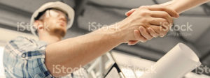 A construction holds blueprints and shake the hand of someone else.
