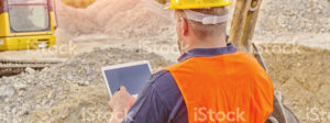 A construction worker reviews plans on tablet at a construction site.