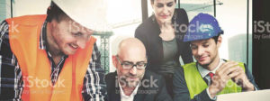 Two construction workers and two business people collaborate over plans on the work site.